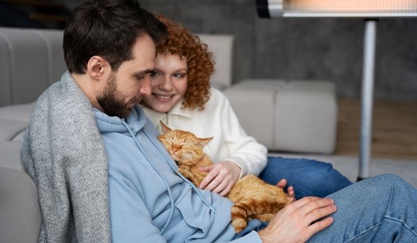 Girl petting her boyfriend’s orange cat sitting in his lap