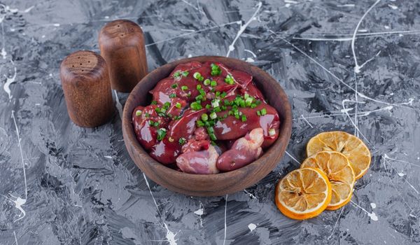 Raw Chicken Liver and Hearts in a Bowl Topped with Spring Onion and Surrounded by Orange Rind and Condiment Bottles on a Grey Slab