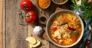 Spicy Chicken Noodle Soup in a Bowl on a Wooden Table Surrounded by Condiments