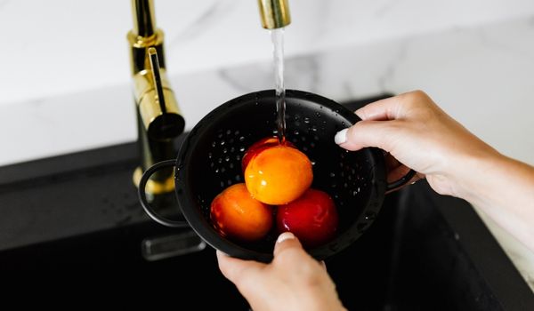 Woman’s hands wash peaches in a black colander