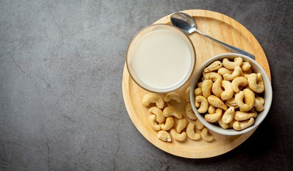 Wooden Snack Tray Carries a Glass of Milk, a Bowl of Cashews, a Spoon, and Some Spare Cashews on a Grey Background