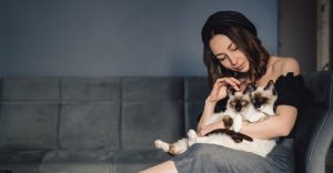 A woman sitting on a sofa holds two Siamese kittens in her lap