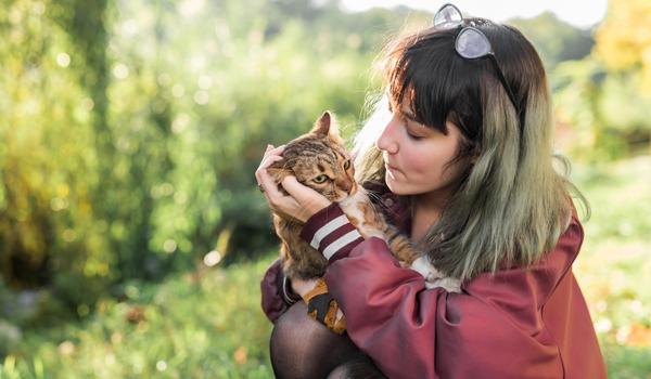 A woman is holding a domestic cat in her arms in a garden
