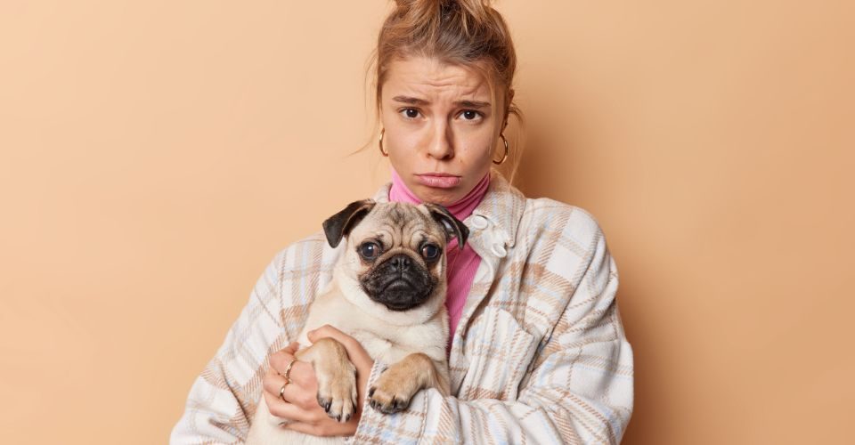 Disappointed frustrated young female dog owner sad holding her pug